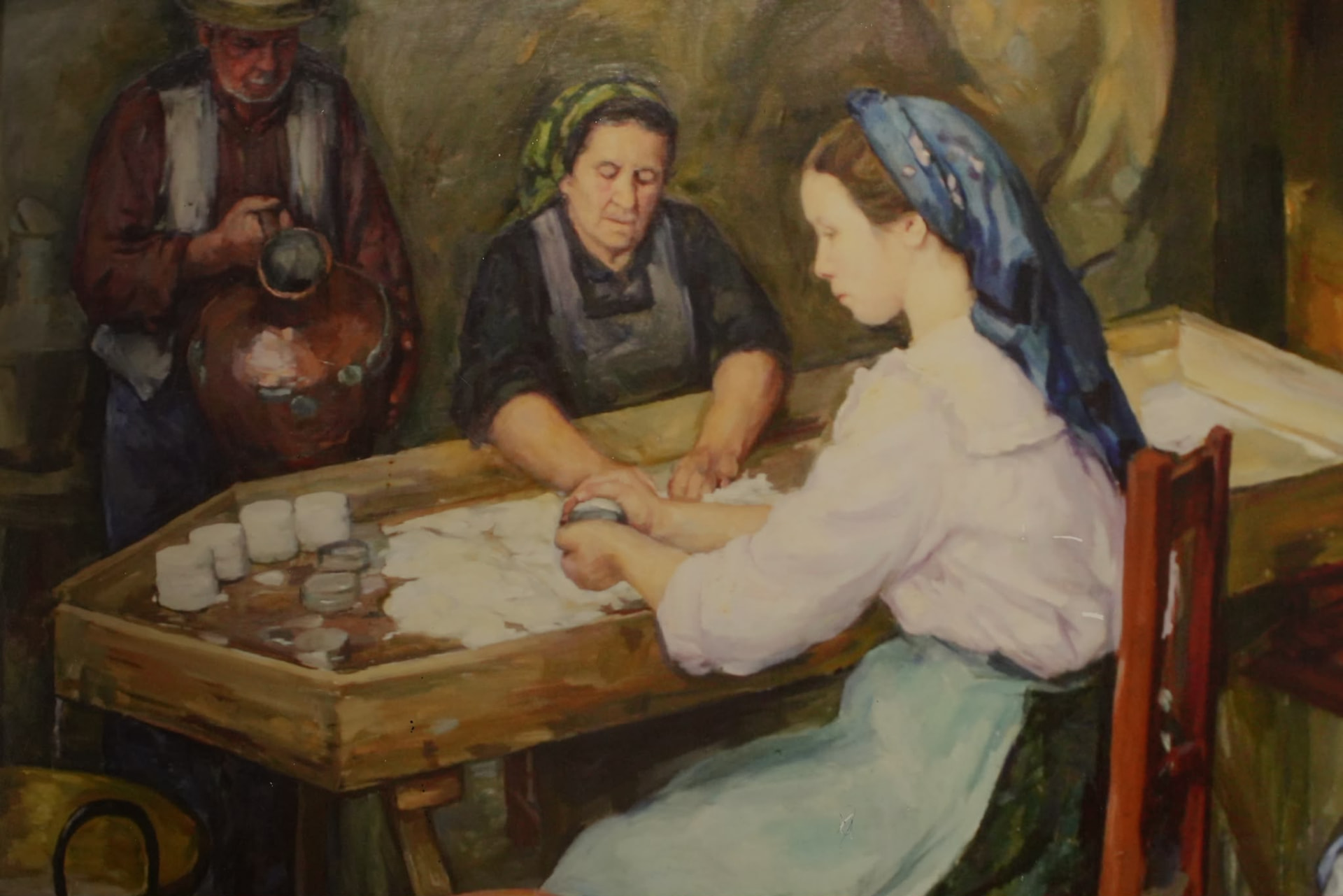 Pintura guardada na queijaria: três pessoas a preparar queijo numa mesa de madeira